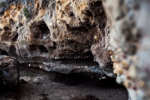 The entrance of a small, dark sandstone cave covered in a variety of tiny naturally embedded pebbles