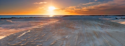 The Sun setting over windswept sand dunes near the coast