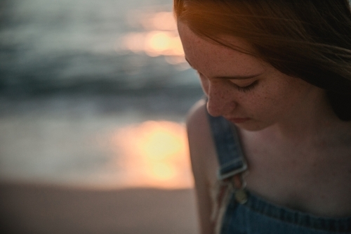 Thoughtful teenage girl on the beach at sunset wearing overalls