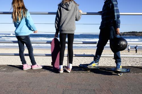 Three kids standing with skateboards looking out at the beach