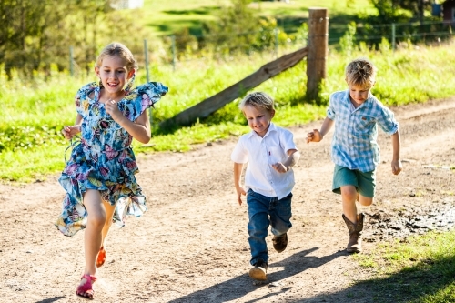 Three siblings running down the farm driveway, playing a game together