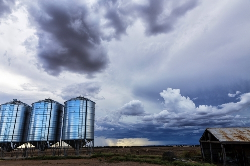 Three silos and an old shed on farm land with storm clouds