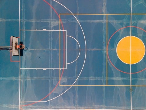 top view shot of a dark blue half basketball court with colorful lines and yellow circle
