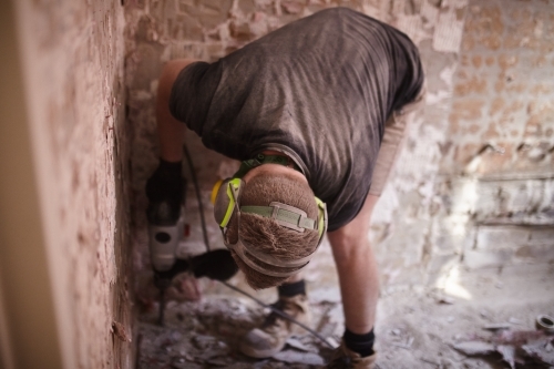 Tradesman jackhammering a floor in  a corner of a room