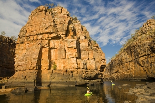 Two canoeists in a gorge with sandstone cliffs and cloud patterns in blue sky