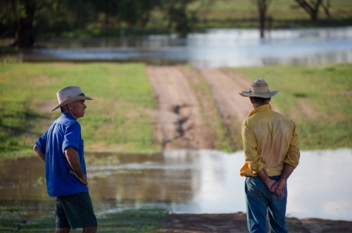Two farmers talking near a flooded creek