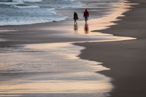 Two figures walking on the beach