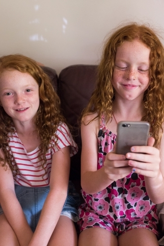 Two girls sitting on a couch playing on a smartphone