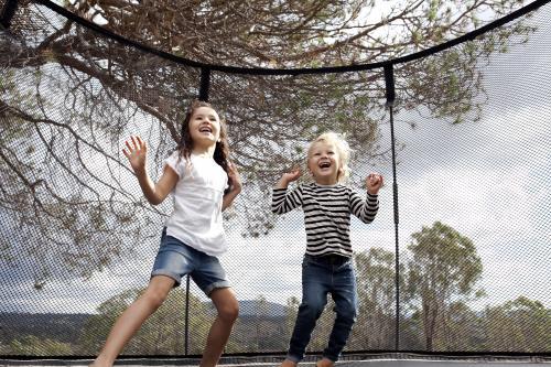 Two happy excited kids jumping on trampoline in backyard