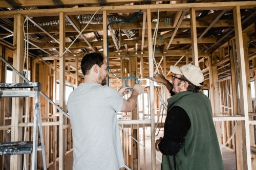 two men are laying cables in a house at frame stage