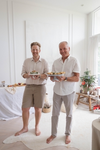 Two men holdig platters of Christmas food