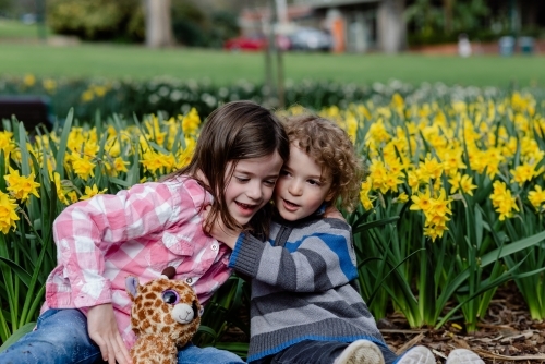 Two young children (brother and sister) playing in front of a daffodil garden
