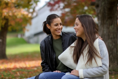 Two young female friends sitting together in an outdoor setting