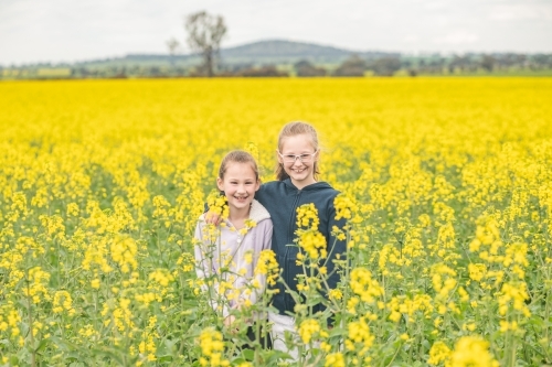 Two young sisters posing in their family canola field.