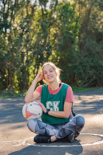 vertical shot of young sporty woman sitting on the ground while touching the ball and her face