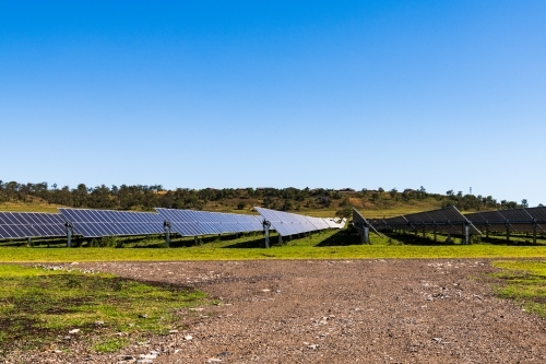 View of gravel road leading to solar panels in rural setting with clear blue sky