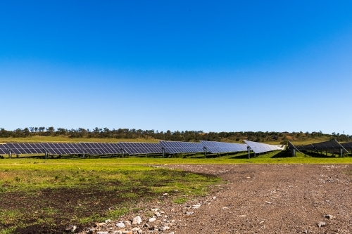 View of large scale solar farm in rural setting with gravel road and clear blue sky