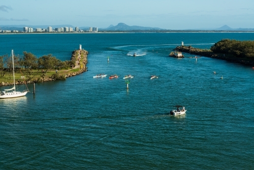 View of river mouth with outrigger canoes training, high rise and mountains in the distance