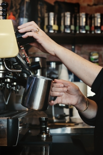 Woman barista making espresso coffee and frothing milk with steam