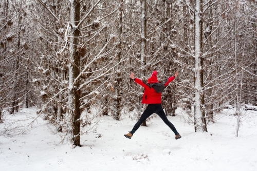 Woman does a star jump in the snow filled pine forest.