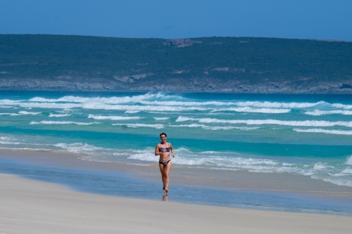 Woman running alone in bikini on remote and rugged coastline
