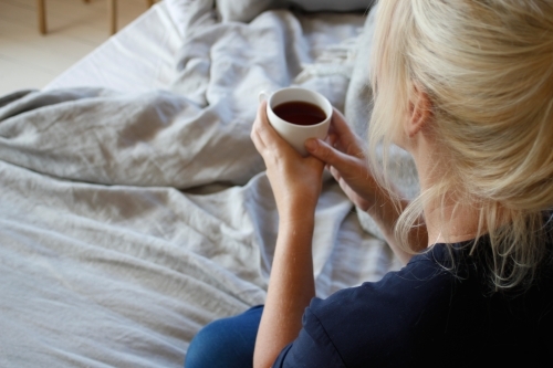 Woman sitting on bed holding cup of tea or coffee