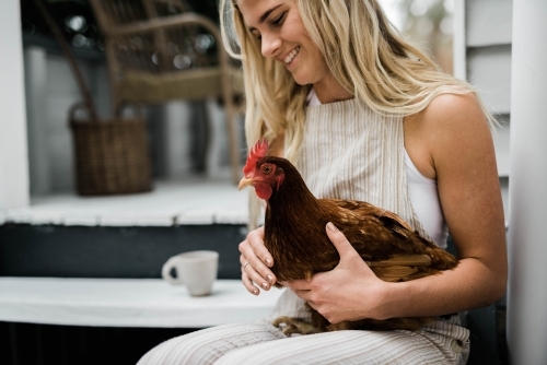 Woman sitting on steps outside home,  holding a chicken