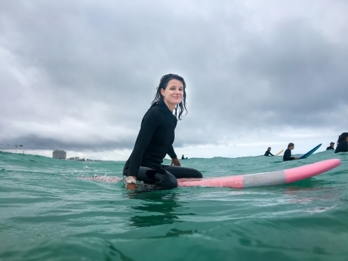 Woman surfer sitting on soft surfboard in ocean looking at camera