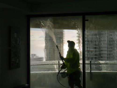 Worker using a pressure hose to clean the windows of an apartment building