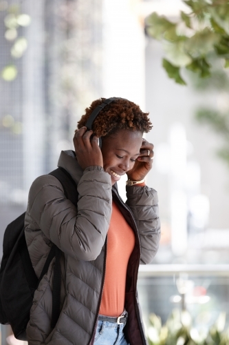 Young African woman listening to music wearing wireless headphones in city
