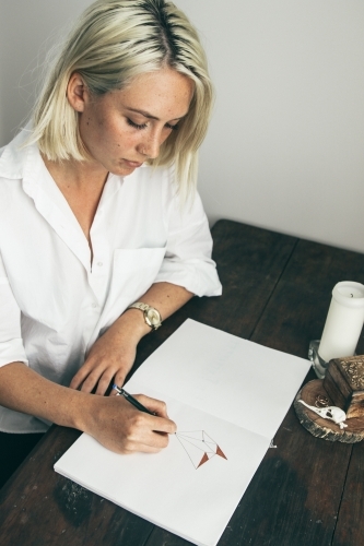 Young blonde woman sitting at desk drawing in a sketch book