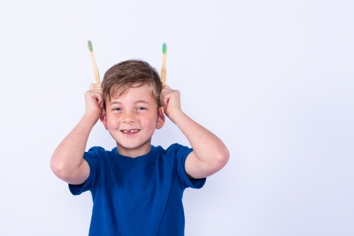 Young boy holding bamboo toothbrushes for ears