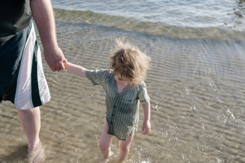 Young boy holding his father's hand while walking in the ocean