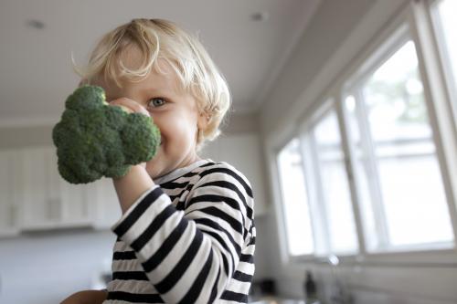 Young boy in kitchen holding broccoli up to face