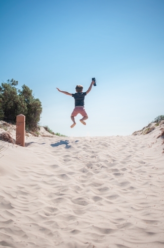 Young boy jumping in the air on white sandy beach