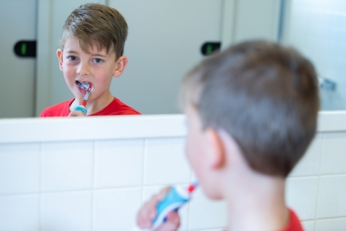 Young boy looking in mirror while cleaning teeth with electric toothbrush