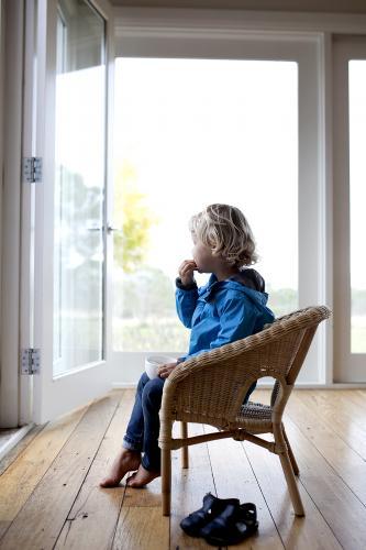 Young boy sitting on chair, eating and looking outside