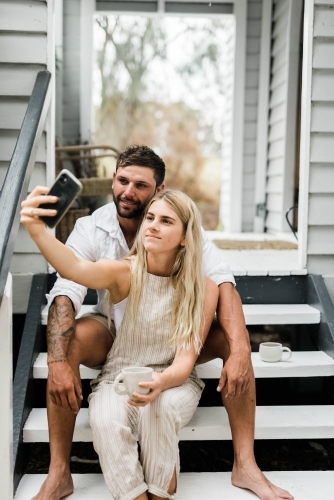 Young couple taking a selfie on the steps of  front porch of weatherboard home