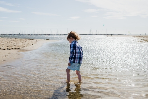Young dressed boy walking in the ocean at St Kilda Beach, Melbourne, Victoria, Australia