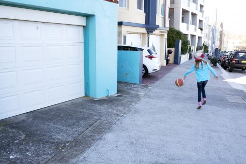 Young girl bouncing basketball down the street