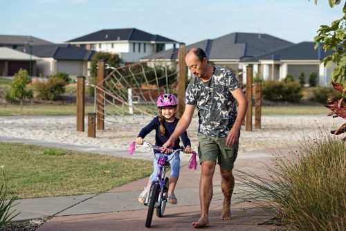 Young girl learning to ride her bike with her dad in the park without training wheels