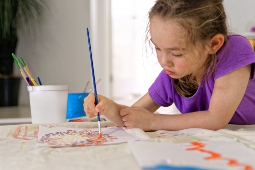 Young girl lying on the floor painting a dot picture with a paint brush