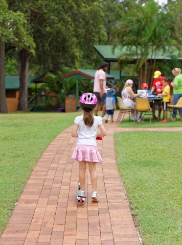 Young girl on scooter wearing helmet watching people playing
