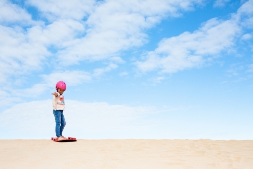 Young girl on top of sand dunes ready to sand board