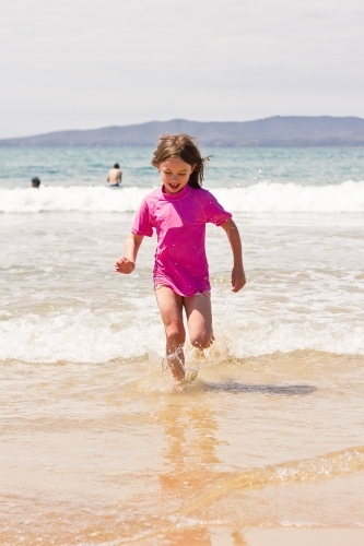 Young girl running through waves at the beach