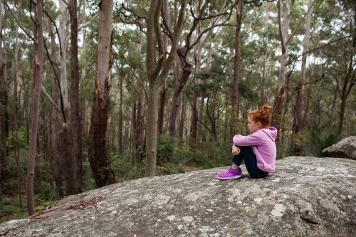 Young girl sitting on a rock with knees bent