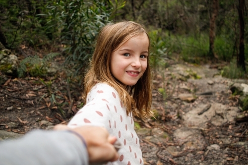 Young girl smiling in the wilderness holding parents hand on an adventure