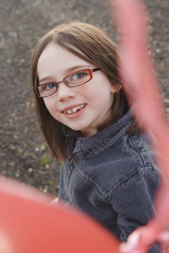 Young girl with glasses and jacket smiling up at camera