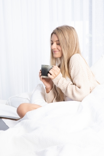 Young lady drinking hot drink in white bed
