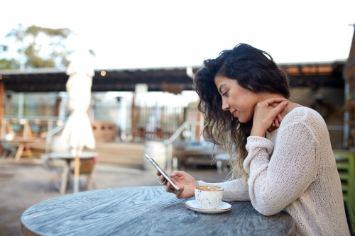 Young middle eastern woman enjoying time on phone at cafe